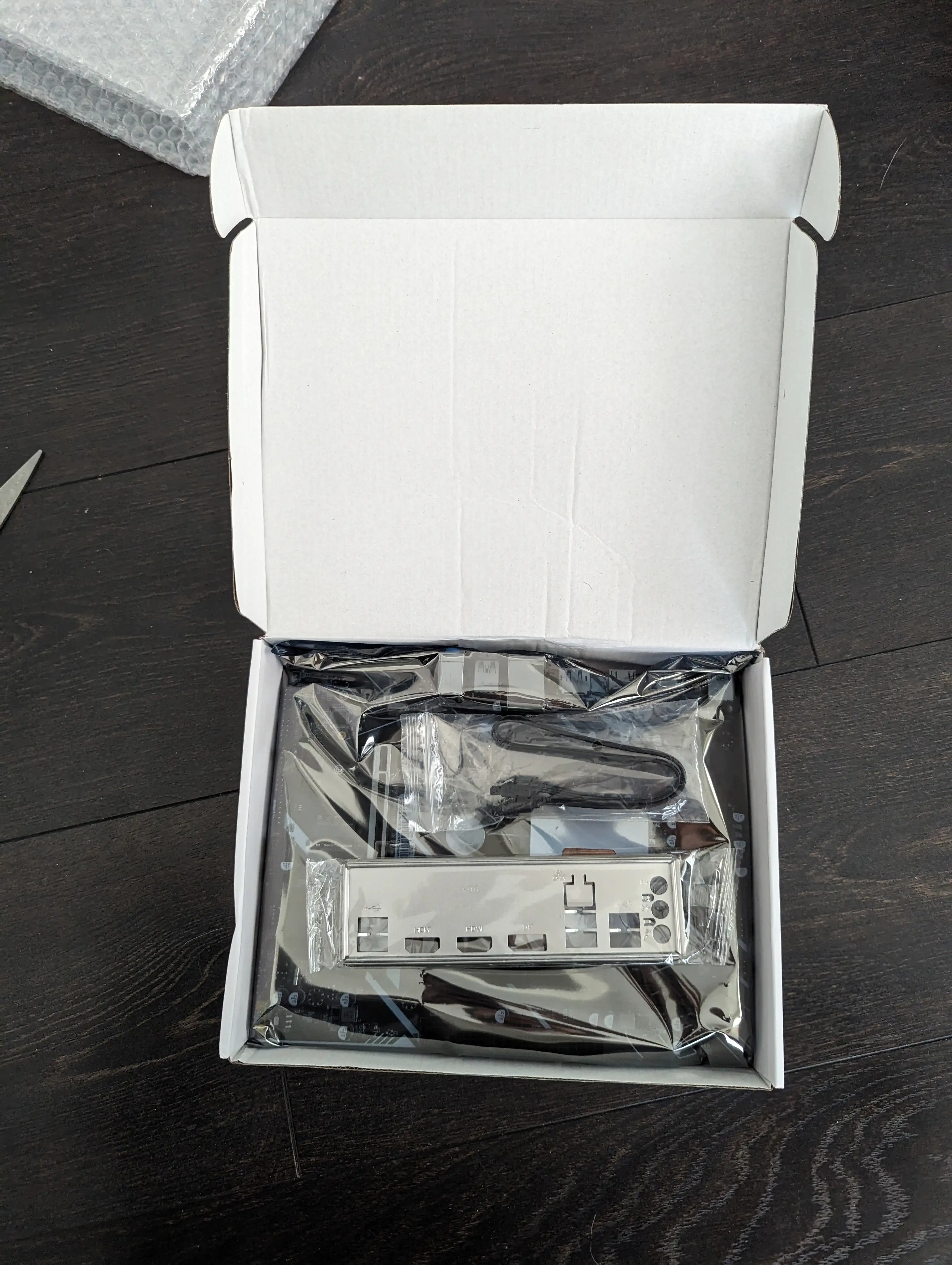A photo showing the inside of an Erying Motherboard box, showing a motherboard packaged in an antistatic bag, a very basic looking IO shield, and a black SATA cable.