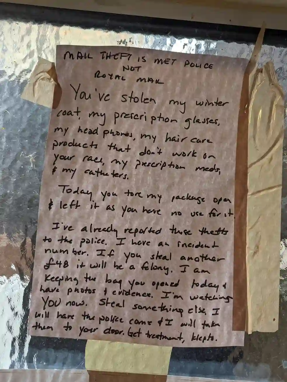 A sign that reads `MAIL THEFT IS MET POLICE NOT ROYAL MAIL. You've stolen my winter coat, my prescription glasses, my headphones, my hair care products that don't work on your race, my prescription meds & my catheters. Today, you tore my package open & left it as you have no use for it. I've already reported these thefts to the police. I have an incident number. If you steal another 48 GBP, it will be a felony. I am keeping the bag you opened today & have photos + evidence. I'm watching YOU now. Steal something else. I will have the police come & I will take them to your door. Get treatment, klepto.`